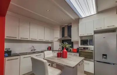 a kitchen with white cabinets and a red vase on a table at Sealax Cottage Fleurpark in Gordonʼs Bay