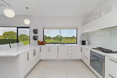 a white kitchen with white cabinets and windows at Sunset Fairway Vista Villa in Cape Town