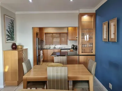 a kitchen and dining room with a wooden table and chairs at Flat 9, Beachfront 2 Bedroom with Sea View for 4 in Gordonʼs Bay