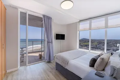 a bedroom with a bed and a balcony with the ocean at Horizon Bay 903 Fresh Beachfront Hideaway in Cape Town