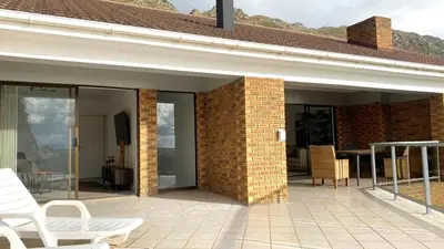 a brick patio with white chairs and a table at Ocean & Mountain View Apartment in Gordonʼs Bay