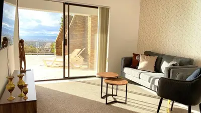 a living room with a couch and a sliding glass door at Ocean & Mountain View Apartment in Gordonʼs Bay