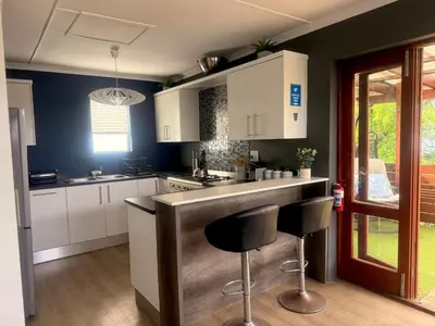 a kitchen with white cabinets and a bar with stools at Loft Escape in Onrus with Hot Tub- 2km from beach in Hermanus