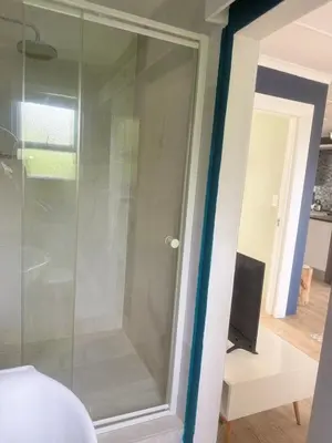 a glass shower door in a room with a television at Loft Escape in Onrus with Hot Tub- 2km from beach in Hermanus