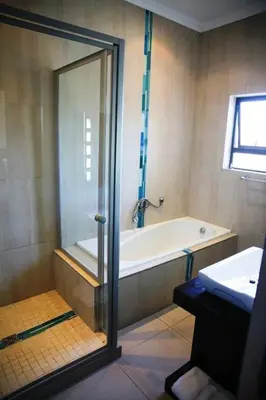 a bathroom with a shower and a tub and a sink at Whalesong Villa in Hermanus