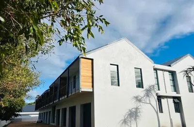 a white house with a balcony and palm trees at Heaven & Earth Apartment 8 in Hermanus