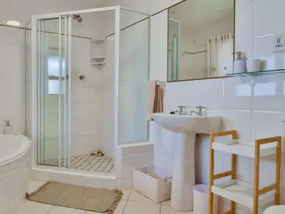 a white bathroom with a shower and a sink at Whales & Wonders Guesthouse in Hermanus