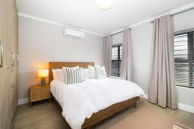 a white bedroom with a bed and a window at Peppertree Villa in Brackenfell