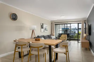 a living room with a wooden table and chairs at Modern 2 Bed Century City Apartment, Pool and Braai in Cape Town