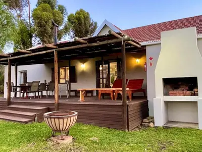 a house with a wooden deck with a table and a grill at Rivergrace Farm in Robertson