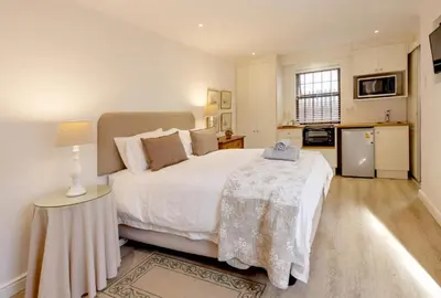 a bedroom with a large white bed and a kitchen at Skye Cottage in Onrus River in Hermanus