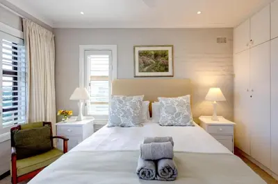 a bedroom with a large white bed and a chair at Skye Cottage in Onrus River in Hermanus