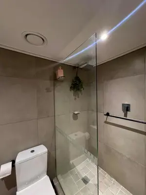 a bathroom with a toilet and a glass shower at Cosy Flat Steps from the Beach in Cape Town