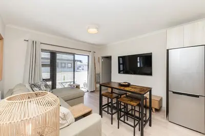 a living room with a table and a refrigerator at Cape On Viola 13-Blouberg Gem Walk to Kite Beach & Ocean Views in Cape Town