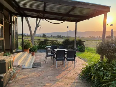 a patio with a table and chairs and the sunset at Leliefontein Eco Cottage and Glamping in Paarl