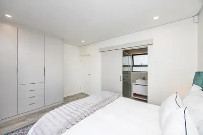 a white bedroom with a bed and a bathroom at Cape Town Bliss in Sandown in Cape Town