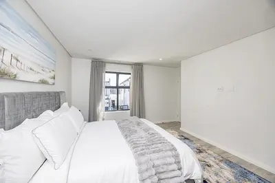 a white bedroom with a large bed and a window at Cape Town Bliss in Sandown in Cape Town