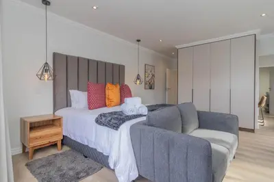 a bedroom with a bed with a couch and a chair at Executive 1 bedroom Cottage, with aircon, king size bed and modern bathroom in Hermanus