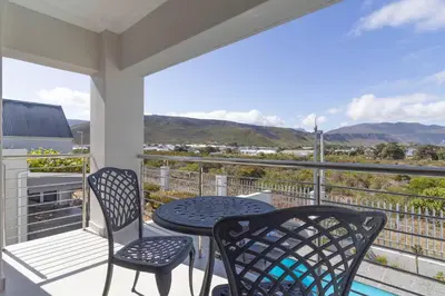 a patio with two chairs and a table on a balcony at Relax in comfort and style with a swimming pool, aircons and braai room in Hermanus