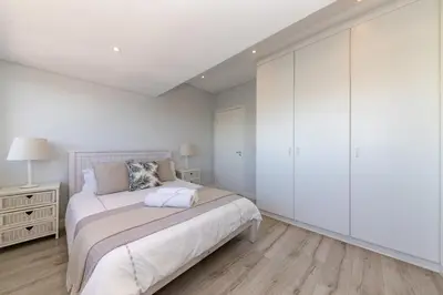 a white bedroom with a bed and white cabinets at Dolphin Beach C110 Beachfront Beauty in Cape Town