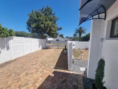 a backyard with a white fence and a brick driveway at Peaceful, Cheerful, Family Friendly 3Bedroom house in Edgemead