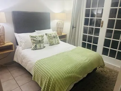 a bedroom with a bed with a green blanket and pillows at The Dragonfly in Paarl