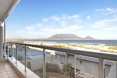 a balcony with a view of the beach and mountains at Dolphin Beach C111 Sea -Table Mountain Views at Dolphin Beach in Cape Town