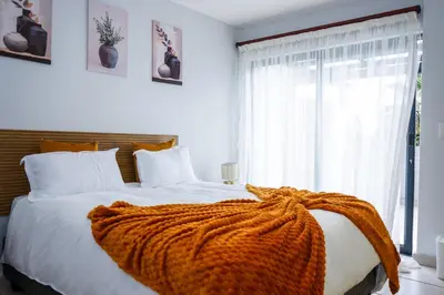 a bedroom with a large bed with an orange blanket on it at Modern 1BR Flat - Near Canal Walk in Cape Town