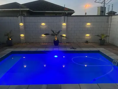 a blue swimming pool with lights on a house at Sunbird Poolhouse in Silver Sands