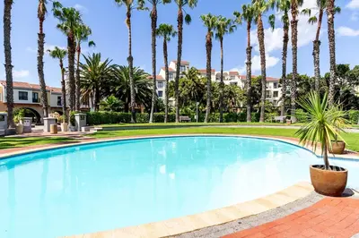 a large swimming pool with palm trees in the background at Luxurious Palm View Apartment Cape Town in Cape Town