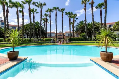 a large pool with palm trees in front of a building at Luxurious Palm View Apartment Cape Town in Cape Town
