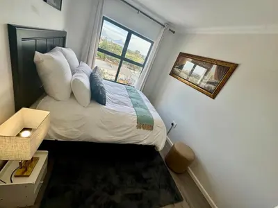 a small bedroom with a bed with pillows and a window at DRJ Luxe Table view in Table View