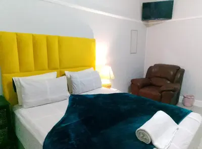 a bedroom with a bed with a yellow headboard and a chair at Goodwood Neo & Ruks guest house in Goodwood