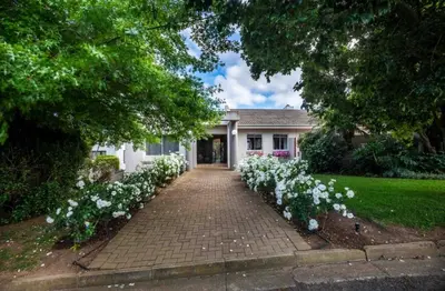 a brick driveway leading to a white house with white flowers at Akasia 1 in Caledon
