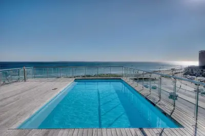 a swimming pool on a deck next to the ocean at Horizon Bay 201-Beachfront Gem Table Mtn in Cape Town
