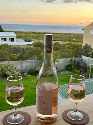 two wine glasses sitting on a table with a bottle of wine at Pebbles & Shells in Kleinmond