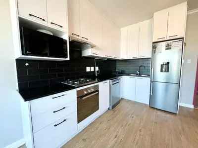 a kitchen with white cabinets and stainless steel appliances at Cape on Porterfield in Cape Town