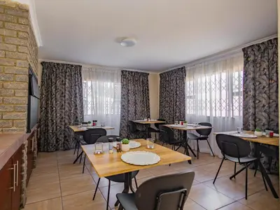 a dining room with tables and chairs and windows at Olive Grove Bed & Breakfast in Kraaifontein