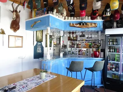 a bar with blue cabinets and two chairs and a table at Big Skies Guesthouse in Gordonʼs Bay