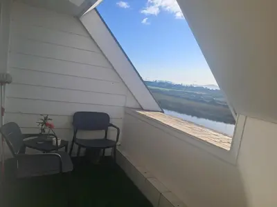 two chairs and a table on a balcony with a window at Salt & Sandy Shores Dolphin Beach Blouberg in Cape Town