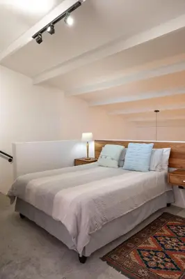 a white bedroom with a large bed with blue pillows at The Glass House Loft in Bettyʼs Bay