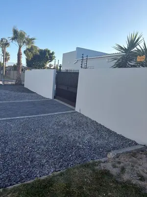 a white fence next to a gravel driveway at Immaculate,Alttrative &Modern 6 minutes away from the beach in Cape Town