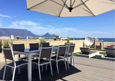 a patio with a table and chairs and an umbrella at Cape Town Sunset Beach Luxury Beachfront Villa in Cape Town