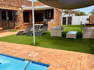 a yard with chairs and an umbrella and a pool at Hideaway-Poolside Comfort cottage 3km to the Beach in Cape Town