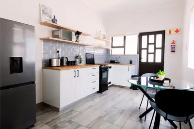 a kitchen with white cabinets and a glass table at Vineyard Flatlets at 13 Olives Estate in Cape Town