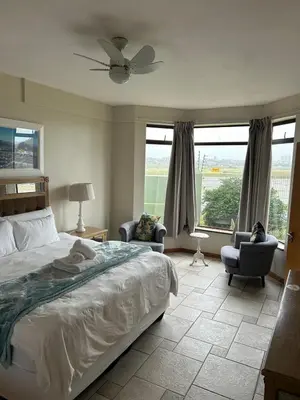 a bedroom with a bed and two chairs and windows at Daisy Accomodation and Spa 5 Bed all private en-suite in Cape Town