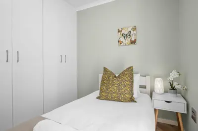 a white bedroom with a bed with a yellow pillow at 17 Megans Place in Bloubergstrand