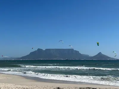 a beach with people in the ocean with mountains in the background at Sea Breeze Kite Dreams 1 in Cape Town