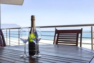 a bottle of wine and two glasses on a wooden table at Beachfront Apt Kite Beach with Table Mtn View Horizon Bay 501 in Cape Town