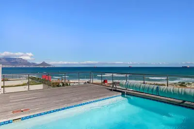 a swimming pool with a boardwalk and the beach at Beachfront Apt Kite Beach with Table Mtn View Horizon Bay 501 in Cape Town